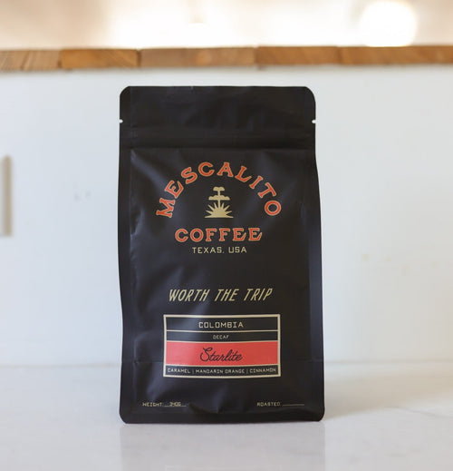A black bag of Mescalito Coffee’s Decaf Whole Coffee Beans | Starlite sits on a white countertop, featuring sugarcane decaf with caramel, mandarin orange, and cinnamon flavor notes.