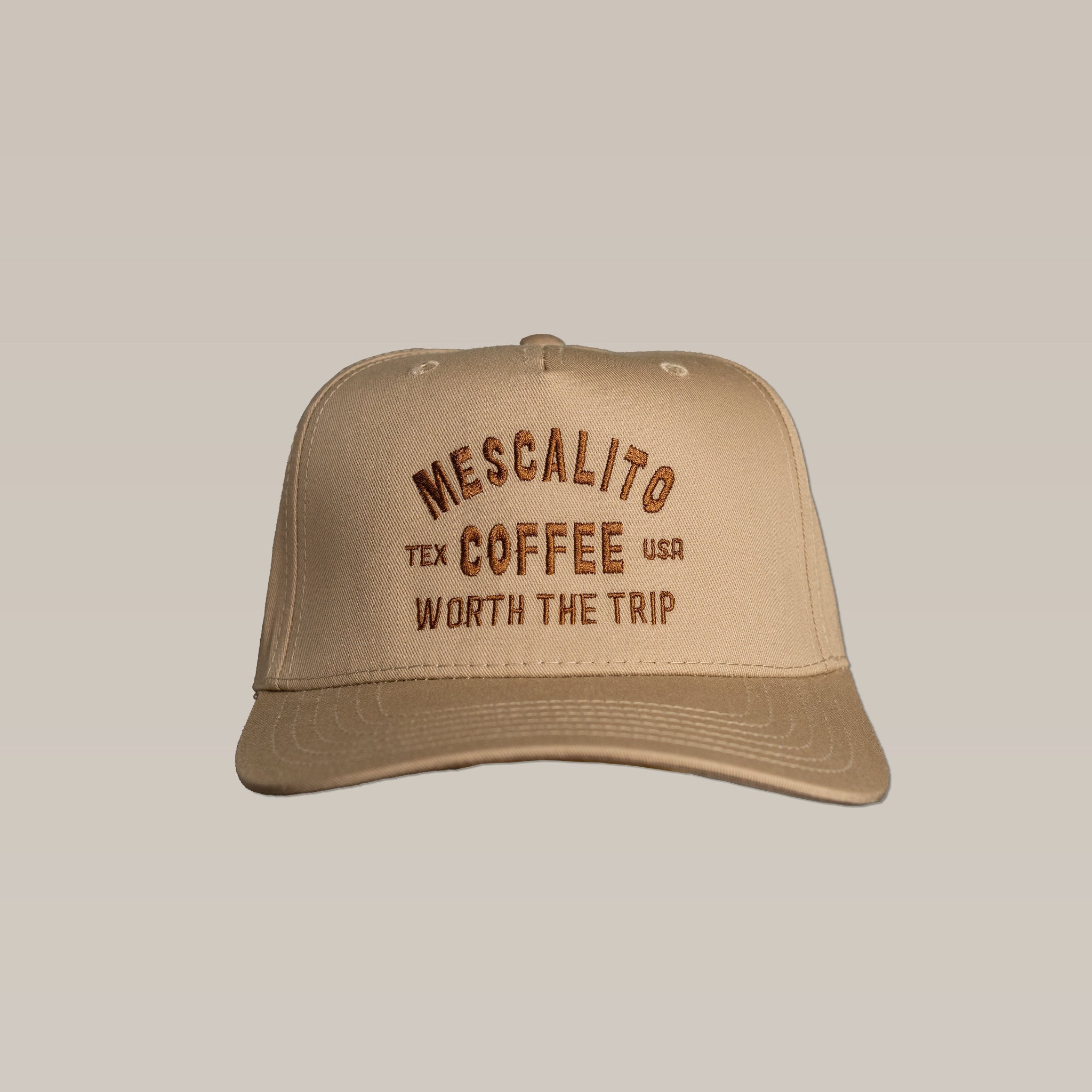 The Shop Hat | Worth The Trip from Mescalito Coffee features tan fabric with "Mescalito Tex Coffee USA Worth the Trip" in brown embroidery—a stylish, laid-back accessory for coffee lovers.